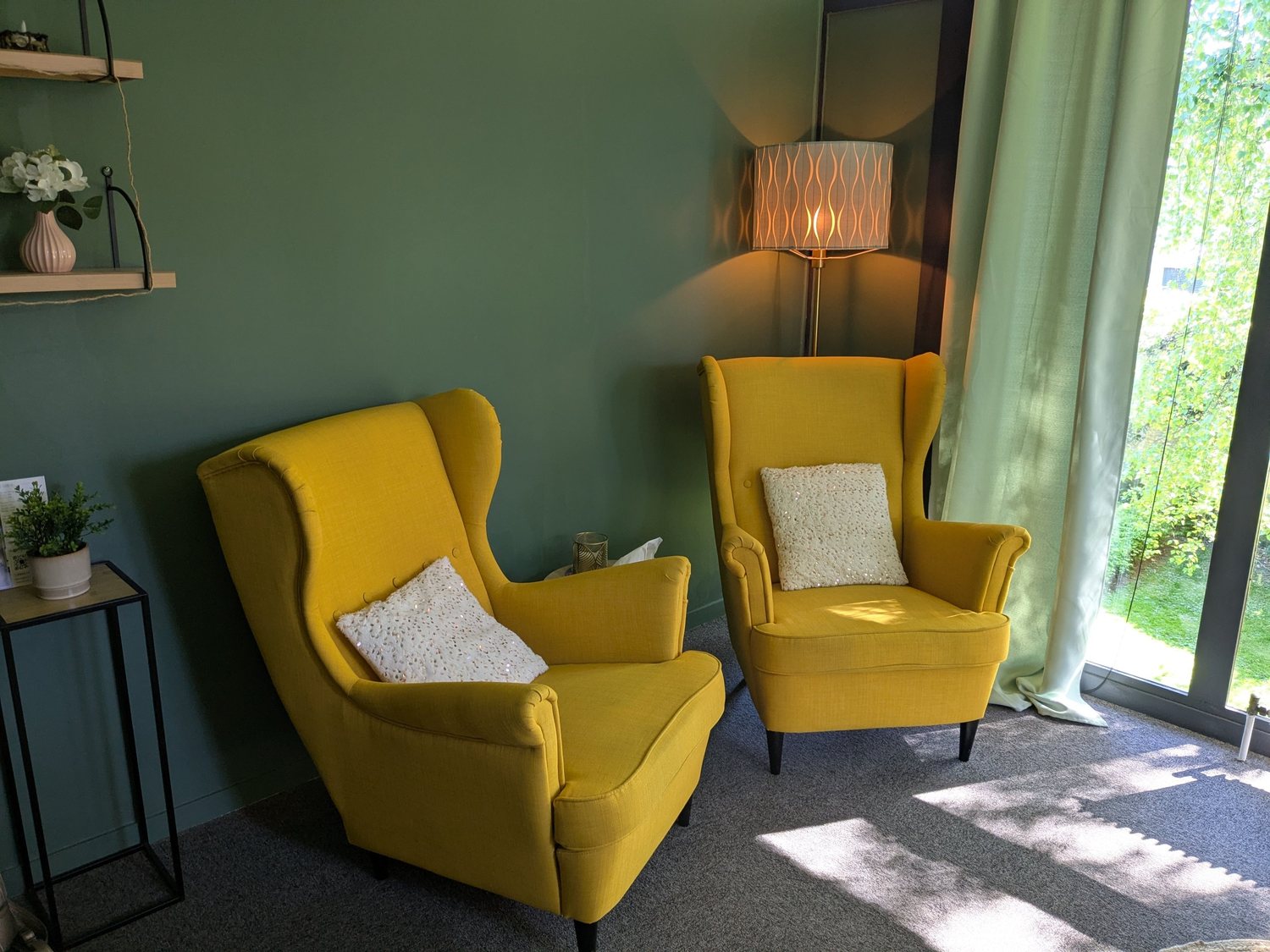 Les deux fauteuils jaunes du cabinet d'Alice Perrin, devant un mur vert et une baie vitrée ouverte sur les arbres