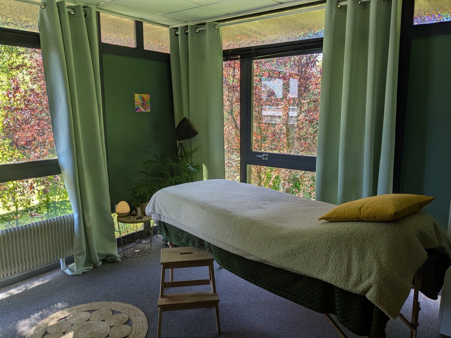 La table de massage du cabinet, habillée de vert, face aux arbres du parc