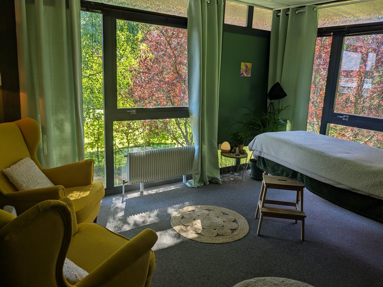Vue de la pièce de soin : fauteuils jaunes, table de massage et baies vitrées sur les arbres